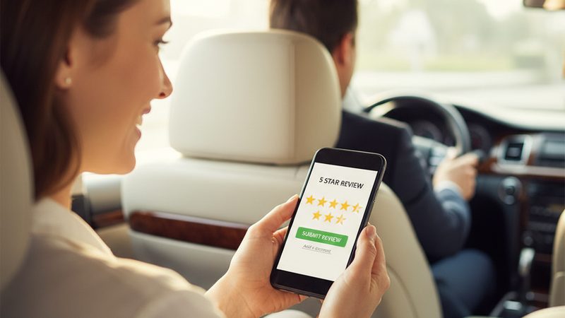 Happy taxi passenger leaving a five-star review on a smartphone inside the back seat of a clean taxi